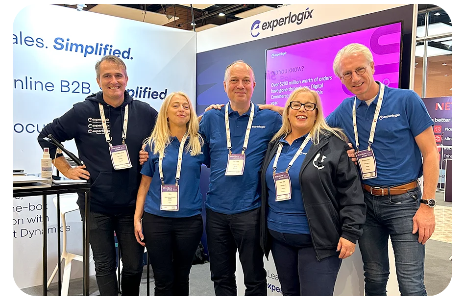 Experlogix employees smiling at a conference in front of a branded booth.